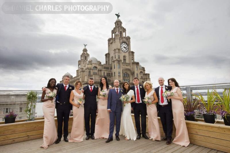 bridal party standing on roof terrace with liver building in background