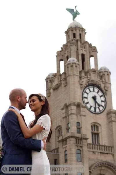 bride and groom embracing with liver building in background