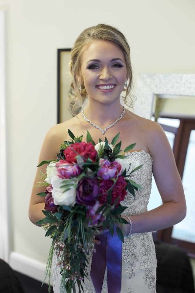 a bride is holding her bridal bouquet up and  smiling at camera