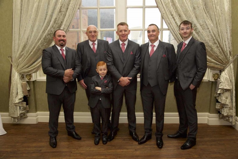 five men and one small boy are standing in a banqueting hall, dressed for a wedding