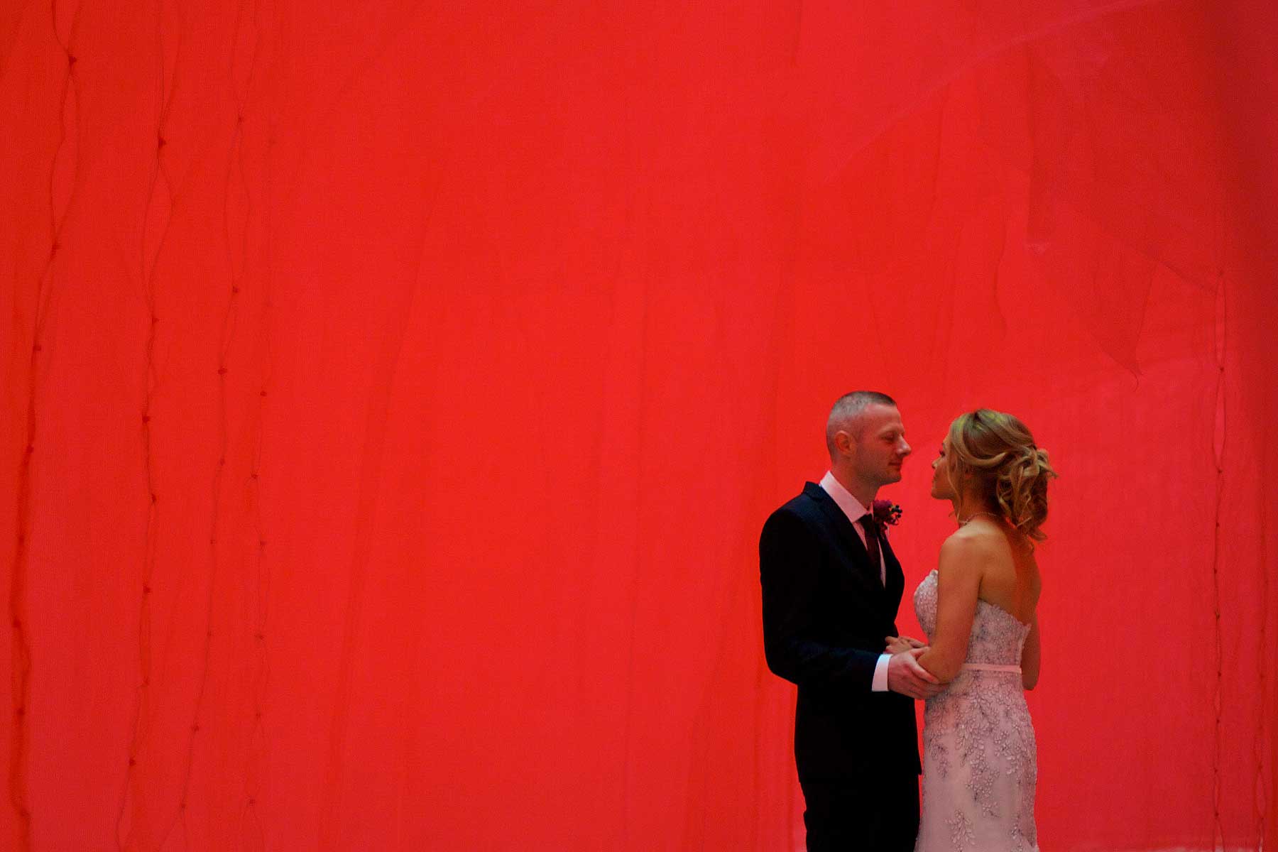 bride and groom standing in front of red cloth