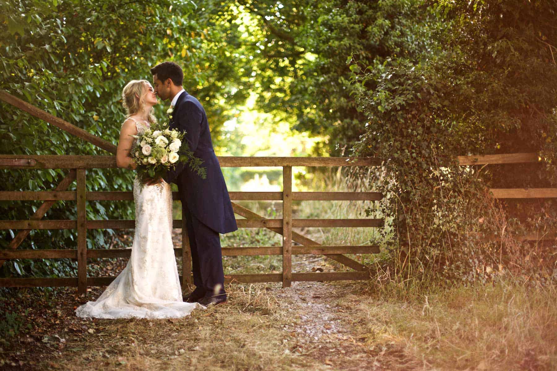 a groom kisses his bride by a farm gate